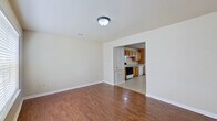 This two-story home offers a practical and well-organized layout across both levels. The entry foyer welcomes you with warm hardwood flooring and a large window that fills the space with natural light. The adjacent living area is open and airy, with the same rich hardwood floors flowing throughout and a direct view into the kitchen through an arched passageway.

The galley-style kitchen is well-appointed with warm oak cabinetry lining both walls, offering generous storage and counter space. White appliances include a refrigerator, electric range, and dishwasher, all set atop light ceramic tile flooring. A dedicated area within the kitchen accommodates a full-size washer and dryer, complemented by a chandelier overhead and a window providing natural light.

A conveniently located bathroom on the main level features tile flooring, a wood-toned vanity with a mirror, and easy accessibility. The second floor houses the bedrooms, each carpeted and equipped with ceiling fans and windows fitted with blinds that allow for ample natural light and outdoor views. The bathroom includes a full-size soaking tub and shower combination with clean white finishes and chrome fixtures. A staircase with wooden treads connects the two floors, completing this functional and comfortable home.