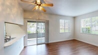 This single-story unit accommodates three bedrooms and one bathroom within a thoughtfully organized floor plan. The combined kitchen and living area serves as the heart of the home, where rich wood-look flooring extends throughout. The living room is bright and open, featuring a ceiling fan with light fixture, a sliding glass door that leads to an outdoor space, and an additional window that draws in natural light and exterior views. A dedicated kitchen area includes warm-toned wood cabinetry, a tile backsplash, white appliances including a refrigerator, electric range, and microwave, along with a sink positioned near a window for added light.

The three bedrooms feature a mix of carpet and wood-look flooring, each equipped with a ceiling fan and windows fitted with blinds. The primary bedroom is a comfortable, well-proportioned space. One bedroom provides direct access to a laundry area. The shared full bathroom is finished with wood cabinetry, a white countertop vanity, a tub-shower combination with sliding glass doors, and wood-look flooring. A hallway connects the rooms efficiently throughout the unit.