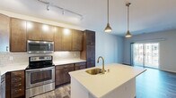 Located on Good Hope Road in Menomonee Falls, Wisconsin, this one-bedroom, one-bathroom residence offers a thoughtfully designed layout across a single floor. The kitchen is a standout feature, showcasing rich, two-tone cabinetry in warm brown tones, white quartz countertops, a subway tile backsplash, and a full suite of stainless steel appliances including a range, built-in microwave, and refrigerator. A central island with an undermount sink and gold-finish faucet is illuminated by modern pendant lighting, complemented by a track lighting system overhead. Durable wood-look flooring runs throughout the main living areas, adding warmth and continuity to the space. The bedroom is generously sized, featuring dual windows with horizontal blinds that allow for ample natural light. A dedicated walk-in closet equipped with wire shelving and hanging rods provides practical storage. The bathroom is finished with a dark-wood vanity, white quartz countertop, a large framed mirror, and a full tub-shower combination, all accented by wood-look tile flooring. The overall design balances contemporary aesthetics with functional, everyday comfort.