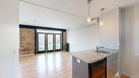 Located at 310 W Sixth St in the heart of Royal Oak, Michigan, this efficiently designed studio seamlessly blends industrial character with modern finishes. The open living area makes a striking first impression with warm hardwood flooring, exposed brick accent walls, and bold navy trim that frames a set of black French doors. These full-length doors invite abundant natural light while offering views of the surrounding neighborhood. Vintage cast-iron radiators on either side of the living space add an authentic industrial charm, while a ceiling fan provides year-round comfort. The kitchen is a functional highlight, centered around a granite-topped island with a stainless steel sink and stylish pendant lighting overhead. White upper cabinetry, stone countertops, and black appliances — including a refrigerator and range — create a clean, contemporary cooking space. A wall-mounted mini-split unit ensures efficient climate control. A separate sleeping area features continuation of the hardwood floors, a ceiling fan, and a sliding-door closet for ample storage. The bathroom is finished with a white vanity, matte black fixtures, and dark tile in the walk-in shower, offering a polished, modern aesthetic. This thoughtfully appointed studio offers an ideal urban living experience in a vibrant Royal Oak location.