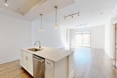 Located at 3400 Sharon Road in Charlotte's SouthPark area, this well-designed one-bedroom, two-bathroom residence offers a thoughtful layout across a single floor. The open-concept living and kitchen area serves as the heart of the home, featuring rich hardwood flooring, track lighting, and a large sliding glass door that floods the space with natural light and provides views of the surrounding neighborhood. The kitchen is equipped with stainless steel appliances, including a range, microwave, and dishwasher, complemented by white cabinetry, subway tile backsplash, a kitchen island with pendant lighting, and sleek countertops. The bedroom features plush carpeting, a tray ceiling, and a large window that brings in generous natural light. An elegant arched alcove adds architectural character to the bedroom space. The primary bathroom is finished with warm stone tile flooring, a dual-sink vanity with white cabinetry and brushed gold fixtures, a soaking tub, and direct access to a dedicated walk-in closet outfitted with a full shelving and organizational system. The hallway connects the rooms with a clean, bright flow, and the overall palette of white walls and neutral tones lends the home a fresh, modern ambiance throughout.