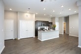 Located at 6840–6846 Governors West NW in Huntsville, Alabama, this single-story unit features a thoughtfully designed open-concept layout that connects the main living areas into a cohesive, functional space. The living room is finished with wood-style plank flooring that extends throughout the main areas, complemented by neutral warm-gray walls and a ceiling fan with integrated lighting. Windows fitted with horizontal blinds allow natural light to filter in, contributing to an open, airy atmosphere.

The kitchen is a standout feature, equipped with dark espresso-toned cabinetry extending to the ceiling for ample storage, granite-style countertops, and a full suite of stainless steel appliances including a refrigerator, electric range, and built-in microwave. A central island with a granite countertop provides additional workspace and casual dining potential, while recessed lighting illuminates the area effectively.

The bedroom is carpeted for comfort, with a generously sized window offering outdoor views and ample natural light. The bathroom includes a full tub-shower combination with built-in shelving, a dark-cabinet vanity with granite countertop, wood-style flooring, and brushed nickel fixtures throughout. A set of double doors near the kitchen provides additional storage space, rounding out this well-appointed unit.