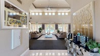 Located at 1601 Vineyard Rd in Roseville, CA, this impressive single-story community clubhouse offers a generous and well-appointed gathering space designed with both style and function in mind. The centerpiece of the facility is a dramatic great room boasting soaring double-height ceilings, rows of clerestory windows that flood the interior with natural light, and elegant arched doorways that lend a refined architectural character. Plush, neutral-toned seating arrangements anchor the lounge area, while large glass doors open directly to an outdoor pool area, seamlessly blending indoor and outdoor living. The connected kitchen features rich dark cabinetry, granite countertops, a tile backsplash, hardwood flooring, and stainless steel appliances — ideal for catering and community events. A breakfast bar provides an open pass-through to the main lounge. The well-equipped fitness center accommodates a full range of cardio and strength training equipment, complemented by floor-to-ceiling mirrors, rubberized flooring, and its own set of clerestory windows. Two private offices, a welcoming entrance, and a pair of connecting hallways round out the layout. Throughout, warm neutral tones, dark carpet with subtle texture, and tasteful décor create a cohesive, upscale ambiance.