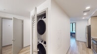 This contemporary high-rise unit showcases a clean, modern aesthetic defined by exposed concrete ceilings and light hardwood flooring throughout. The open living area is anchored by large floor-to-ceiling windows that frame expansive city views, filling the space with natural light and a strong urban connection. A comfortable seating arrangement and dining area flow naturally into a well-appointed kitchen, which features light wood cabinetry, white quartz countertops, and a full suite of stainless steel appliances including a refrigerator, range, microwave, and dishwasher.

The bedrooms continue the industrial-modern design language, each offering exposed concrete ceilings, generous floor-to-ceiling windows with dynamic urban vistas, open closets with hanging rods, and built-in bed frames with integrated drawer storage. The shared bathroom is thoughtfully designed with a dual-sink vanity, light wood cabinetry, a wide wall mirror with integrated lighting, and white quartz countertops that echo the kitchen's palette.

A dedicated in-unit laundry closet houses a stacked washer and dryer, adding everyday convenience. Throughout the unit, the consistent use of natural materials, neutral tones, and large-format glazing creates a cohesive, light-filled living environment with a distinctly contemporary character.