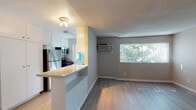 Located on Weddington Street in the Sherman Oaks neighborhood of Los Angeles, this single-floor unit offers a practical and well-appointed layout designed for comfortable everyday living. The open-concept living and kitchen area forms the heart of the space, where a peninsula counter with a light stone surface separates the two zones while maintaining a sense of openness. The kitchen is equipped with stainless steel appliances, including a refrigerator and gas range, complemented by ample white cabinetry that extends to the ceiling for generous storage. Light wood-style flooring runs throughout the main living areas, lending warmth and visual continuity. A large window in the living area allows natural light to pour in, with views of surrounding greenery providing a pleasant outdoor connection. A wall-mounted air conditioning unit ensures year-round climate comfort. The bathroom features a clean, functional design with a shower-tub combination, wood-style flooring, and stone-topped vanity. A separate bedroom area offers a spacious, open feel with a textured ceiling, neutral-toned walls, and a closet with louvered doors. The overall ambiance is bright, clean, and move-in ready, making this a straightforward and functional space in a well-situated Los Angeles location.