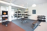 Located at 2204 Duluth Highway 120 in Duluth, Georgia, this single-floor fitness center is a comprehensive facility designed to support a wide range of workout routines. The space is organized into distinct training zones, each tailored to specific fitness disciplines.

The cardio area anchors one side of the facility, featuring a row of treadmills and elliptical machines positioned directly in front of large, floor-to-ceiling windows. These expansive windows flood the space with natural light and offer views of the surrounding outdoor amenities and greenery, creating an energizing atmosphere for exercise.

Adjacent to the cardio zone is a strength and functional training area equipped with a multi-station cable machine, a comprehensive functional rig loaded with kettlebells, medicine balls, battle ropes, TRX suspension trainers, and weight plates. A dedicated free weights section includes a full rack of dumbbells, an adjustable bench, and exercise mats, providing ample options for resistance training.

Additional strength machines, including a leg extension and curl unit, are positioned near windows overlooking a landscaped outdoor terrace. Floor-to-ceiling mirrors line portions of the walls, visually expanding the space and assisting with form during workouts.

The flooring transitions between carpet, rubber, and hardwood-style surfaces to suit different training needs. Recessed lighting, ceiling fans, and exposed ductwork contribute to the facility's modern, functional aesthetic throughout.