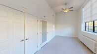 Located at 403 Dillard School Dr in Yanceyville, NC, this single-floor, one-bedroom, one-bathroom unit offers an efficiently designed layout with impressive architectural details. The open-concept living, dining, and kitchen area is a standout, featuring notably high ceilings that amplify the sense of space. A large bank of black-framed windows lines the living area, inviting abundant natural light and outdoor views, complemented by ceiling fans and roller shades for comfort and privacy. A vintage-style cast iron radiator adds a charming architectural detail beneath the windows.

The kitchen is well-appointed with gray shaker-style cabinetry, light countertops, black appliances including a range and refrigerator, and a central island with a double stainless steel sink and pendant lighting overhead—ideal for both cooking and casual dining.

The bedroom is a comfortable, carpeted retreat with soaring ceilings, a ceiling fan, and two closets for ample storage. The full bathroom features accessibility-friendly grab bars and a tub/shower combination. A dedicated laundry area and additional electrical panel closet round out the practical features of this well-designed unit.