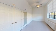 Located at 403 Dillard School Dr in Yanceyville, NC, this single-floor, one-bedroom, one-bathroom unit offers an efficiently designed layout with impressive architectural details. The open-concept living, dining, and kitchen area is a standout, featuring notably high ceilings that amplify the sense of space. A large bank of black-framed windows lines the living area, inviting abundant natural light and outdoor views, complemented by ceiling fans and roller shades for comfort and privacy. A vintage-style cast iron radiator adds a charming architectural detail beneath the windows.

The kitchen is well-appointed with gray shaker-style cabinetry, light countertops, black appliances including a range and refrigerator, and a central island with a double stainless steel sink and pendant lighting overhead—ideal for both cooking and casual dining.

The bedroom is a comfortable, carpeted retreat with soaring ceilings, a ceiling fan, and two closets for ample storage. The full bathroom features accessibility-friendly grab bars and a tub/shower combination. A dedicated laundry area and additional electrical panel closet round out the practical features of this well-designed unit.