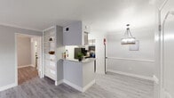 This single-floor Houston residence presents a cohesive, modern design defined by a neutral gray-and-white palette and light wood-style flooring that runs throughout. The open-concept living area is bright and airy, featuring crown molding, large baseboards, and a sliding glass door fitted with vertical blinds that invites natural light and provides outdoor access. A stylish pendant chandelier serves as a focal point in the adjoining dining area.

The kitchen is efficiently designed in a galley configuration, offering granite countertops, gray cabinetry with updated hardware, a tile backsplash, stainless steel sink with a modern faucet, and black appliances including a range and refrigerator. An industrial-style pendant light illuminates the workspace. A peninsula with matching granite countertops separates the kitchen from the living area, complemented by a built-in white open shelving unit that adds both storage and visual interest.

The bedroom is a calm, well-proportioned space with a window allowing natural light and a ceiling light fixture. The bathroom features large-format tile in the tub/shower surround, accented by a decorative mosaic tile border, paired with a granite-topped vanity and wood-style flooring, creating a polished, cohesive finish.