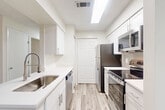Located at 12505 Loston Cir in Fairfax, Virginia, this well-appointed one-bedroom, one-bathroom residence offers a thoughtfully designed layout with a clean, modern aesthetic throughout. Light-toned luxury vinyl plank flooring flows seamlessly across all rooms, enhancing the bright and airy atmosphere created by neutral white and soft beige walls.

The galley-style kitchen is a functional highlight, featuring white shaker cabinetry, white quartz countertops, a stainless steel sink with a pull-down faucet, and a full suite of stainless steel appliances including a refrigerator, electric range, microwave, and dishwasher. A peninsula with additional counter space connects the kitchen to the open living and dining area, which benefits from natural light through large windows with views of surrounding greenery. A private balcony is accessible directly from the living area.

The spacious bedroom offers a generous footprint, natural light from a large window, and convenient access to multiple closets. The full bathroom is finished with crisp white tile surrounding the tub-shower combo, complemented by a vanity and wood-look flooring. Additional practical features include a dedicated laundry area, a pantry, and ample closet storage throughout. A hallway connects the main spaces for an efficient and comfortable flow.