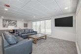 Located at The Core Apartments in Nampa, Idaho, this single-floor amenity space is designed to provide residents with a well-rounded communal environment. The main area is bright and open, featuring patterned carpet flooring, a drop tile ceiling with recessed lighting, and multiple large windows that invite natural light while offering views of the surrounding exterior. The lounge area is furnished with plush gray leather sofas arranged around a wooden coffee table, alongside a wall-mounted flat-screen television — ideal for relaxed social gatherings. Adjacent to the lounge, a dining area accommodates a full-sized table with seating for multiple guests, providing a comfortable space for shared meals or group meetings. A built-in kitchenette lines one wall, outfitted with an extended run of warm wood cabinetry, a white countertop workspace, a compact refrigerator, and a sink, making the space well-suited for hosting events or casual get-togethers. A dedicated private office off the main area offers a quiet workspace, equipped with an L-shaped built-in desk, a computer workstation, and a wall-mounted mini-split HVAC unit for individualized climate control. Together, these spaces deliver a clean, modern, and highly functional amenity suite for residents of The Core Apartments.