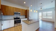 Located at 1100 S Public Rd in Lafayette, Colorado, this single-floor unit offers a thoughtfully designed open-concept layout with modern finishes throughout. The kitchen serves as the heart of the space, showcasing warm wood cabinetry, crisp white lower cabinets, and a classic subway tile backsplash. A generously sized center island with a quartz-style countertop and undermount sink provides ample prep space and is illuminated by a trio of amber pendant lights. Stainless steel appliances — including a refrigerator, range, microwave, and dishwasher — complete the well-equipped kitchen. Light wood flooring flows throughout the main living areas, enhancing the bright, airy ambiance. The living area features a ceiling fan and a glass door that opens to an outdoor space, inviting natural light deep into the unit. The bedrooms offer plush carpeting, large windows with exterior views, and generous closet space, including a walk-in closet in the primary bedroom. A clean, modern bathroom features a tiled tub-shower combination, wood-tone flooring, and chrome fixtures. Overall, the unit presents a cohesive, contemporary aesthetic with an emphasis on functionality and natural light.