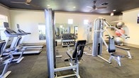 This fitness center is designed to support a comprehensive workout experience within a single-level layout. The space is outfitted with a robust selection of professional-grade equipment, including Inflight Fitness strength machines, a multi-station cable system, and an organized free weight rack stocked with a full range of dumbbells. Full-length mirrors line the walls, enhancing the sense of space and allowing users to monitor their form during exercises. The flooring features a durable, textured carpet-style surface suited for gym use, providing comfort and stability underfoot. Recessed lighting in the ceiling ensures the space is well-lit throughout, while a ceiling fan promotes air circulation for a more comfortable workout environment. Small windows positioned near the ceiling allow for additional natural light. The overall layout is thoughtfully arranged to provide ample room between equipment, facilitating safe and efficient movement throughout the space. The neutral color palette and clean design give the fitness center a functional yet welcoming ambiance, making it a practical and well-appointed facility for strength training and general fitness.