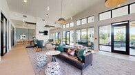 Located at 1830 Homerun Rd in Kissimmee, Florida, this single-floor community clubhouse spans a generously sized footprint designed to accommodate a variety of social and professional activities. The architecture is defined by soaring double-height ceilings, white shiplap paneling, and floor-to-ceiling black-framed windows that flood the interior with natural light and offer sweeping views of the surrounding outdoor landscape and pool area.

The open lounge area serves as the heart of the space, furnished with a tufted leather sofa, teal accent chairs, patterned ottomans, and layered area rugs atop polished concrete flooring. Pendant lighting adds warmth throughout. A built-in counter along the window wall provides bar-height seating, ideal for casual work or socializing.

A dedicated café-style dining nook features built-in banquette seating set against a striking chevron-patterned blue accent wall, complemented by pendant lighting and contemporary artwork. A large communal table with leather bar stools sits beneath a bold dome pendant, with a wall-mounted TV and exposed brick wall nearby.

Private, glass-enclosed work pods — named "Queen Palms" and "Lady Palms" — offer focused workspace, each appointed with tropical botanical wallpaper, carpeted flooring, and built-in desks. A larger glass-walled conference room accommodates collaborative meetings. Sliding glass doors open directly to an outdoor terrace, seamlessly connecting interior and exterior amenity spaces.