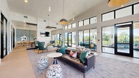 Located at 1830 Homerun Rd in Kissimmee, Florida, this single-floor community clubhouse spans a generously sized footprint designed to accommodate a variety of social and professional activities. The architecture is defined by soaring double-height ceilings, white shiplap paneling, and floor-to-ceiling black-framed windows that flood the interior with natural light and offer sweeping views of the surrounding outdoor landscape and pool area.

The open lounge area serves as the heart of the space, furnished with a tufted leather sofa, teal accent chairs, patterned ottomans, and layered area rugs atop polished concrete flooring. Pendant lighting adds warmth throughout. A built-in counter along the window wall provides bar-height seating, ideal for casual work or socializing.

A dedicated café-style dining nook features built-in banquette seating set against a striking chevron-patterned blue accent wall, complemented by pendant lighting and contemporary artwork. A large communal table with leather bar stools sits beneath a bold dome pendant, with a wall-mounted TV and exposed brick wall nearby.

Private, glass-enclosed work pods — named "Queen Palms" and "Lady Palms" — offer focused workspace, each appointed with tropical botanical wallpaper, carpeted flooring, and built-in desks. A larger glass-walled conference room accommodates collaborative meetings. Sliding glass doors open directly to an outdoor terrace, seamlessly connecting interior and exterior amenity spaces.