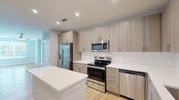 Located at 4710 Mint Leaf Ln in Raleigh, NC, this single-floor home offers a clean, contemporary design with a cohesive aesthetic throughout. The kitchen is a standout feature, showcasing light wood-tone cabinetry that extends floor to ceiling, crisp white quartz countertops, a full suite of stainless steel appliances including a side-by-side refrigerator with water dispenser, electric range, built-in microwave, and dishwasher. A central island provides additional prep and counter space, while recessed lighting illuminates the area effectively. Light hardwood flooring flows throughout the main living areas, complementing the soft gray walls and white trim that give the home a bright, neutral palette. The living spaces are generously proportioned, with large windows fitted with white blinds that invite natural light and offer views of the surrounding greenery. Bedrooms are carpeted and well-lit, each featuring windows with outdoor views and access to closet space. The bathroom is finished with a tiled tub-shower combination, a wood-toned vanity with white countertop, a large mirror, and modern brushed nickel fixtures. The entryway provides convenient storage with built-in closet access. Overall, the home presents a polished, move-in-ready interior suited for comfortable everyday living.
