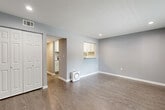 This single-floor unit offers a thoughtfully designed layout comprising a combined kitchen and living area, one bedroom, one bathroom, and a hallway. Throughout the space, wood-look laminate flooring and cool gray-toned walls establish a clean, cohesive aesthetic complemented by white trim and recessed lighting.

The open living area is generously sized, featuring a built-in closet with bifold doors and a pass-through window connecting directly to the kitchen, enhancing the sense of openness between the two spaces. The kitchen is well-equipped with white shaker-style cabinetry, granite-look countertops, stainless steel appliances including a range, microwave, dishwasher, and refrigerator, and light-toned flooring.

The spacious primary bedroom accommodates a ceiling fan, a closet, a window with outdoor views and natural light, and direct access to the bathroom. The bathroom features wood-plank tile flooring, a white vanity with a stone-topped countertop, a framed mirror, and a tiled shower-tub combination, delivering a clean and updated finish throughout.