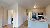 This well-designed single-floor unit offers a practical and modern layout that maximizes every inch of available space. The open-concept kitchen anchors the living area and features light wood cabinetry, a black appliance suite including a full-size refrigerator, electric range, and over-the-range microwave, as well as a peninsula with a stainless steel sink and countertop seating. Light-toned luxury vinyl plank flooring runs continuously throughout, lending warmth and visual cohesion to the space.

The main living area is bright and airy, benefiting from a sliding glass door that brings in natural light and provides outdoor access. A ceiling fan overhead adds to the comfort of the room, while a built-in Murphy bed with integrated shelving and drawer storage offers a versatile and space-efficient sleeping solution.

A dedicated laundry closet, accessible via bifold doors, houses a full-size washer and dryer, conveniently located adjacent to the kitchen. The bathroom is finished with patterned decorative floor tile, a full soaking tub with shower, and clean white walls that create a crisp, functional atmosphere. Additional storage and utility access panels are tucked neatly into the hallway. The overall design is clean, contemporary, and thoughtfully arranged for comfortable everyday living.