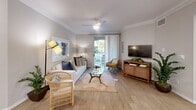 Located at 1001 Starbuck St in Fullerton, CA, this well-appointed one-bedroom, one-bathroom residence offers a thoughtfully designed single-floor layout. The open-concept living and kitchen area forms the heart of the home, featuring wood-look flooring, crown molding, and a ceiling fan that enhances airflow and comfort. The living room provides ample space for relaxing and entertaining, with a sliding glass door leading to a private balcony overlooking lush, mature trees and manicured landscaping. The kitchen is outfitted with stainless steel appliances, white shaker cabinetry, a central island with pendant lighting, a glass block window for natural light, and a dedicated dining area. The bedroom is a comfortable retreat, highlighted by a bold accent wall, plush carpeting, natural light from a large window, and direct access to a spacious closet. The bathroom features a white vanity with dual mirrors, a well-lit vanity fixture, and clean, neutral finishes. A hallway connects the main living areas to the private spaces, completing the efficient and functional floor plan. The balcony offers a serene outdoor escape with views of greenery and the surrounding community streetscape.