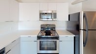 This 2-bedroom, 2-bathroom unit showcases a contemporary industrial aesthetic carried consistently throughout the space. Polished concrete floors run throughout, lending a sleek, urban character that pairs well with the crisp white walls and dark-framed accents found across the unit.

The kitchen is outfitted with stainless steel appliances, including a range, oven, and over-the-range microwave, complemented by clean white cabinetry and light-toned countertops that create a bright, functional workspace.

The bedrooms are generously proportioned, each offering ample closet space with sliding panel doors. Exposed ductwork and industrial-style ceiling fixtures add to the loft-like ambiance, while large windows invite natural light and offer city views.

The two bathrooms are finished with a clean, modern sensibility. The primary bathroom features a wide vanity with a white countertop, undermount sink, and contemporary light fixtures above a large mirror, along with sleek cabinetry in a soft grey tone. The second bathroom includes a full tub-shower combination with white tile surround and chrome fixtures.

The overall layout is practical and open, with a logical flow between living areas, bedrooms, and bathrooms, making this a well-designed urban residence with strong industrial-modern character throughout.