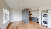 Located at 1341 N Killingsworth St in Portland's Piedmont neighborhood, this thoughtfully designed unit offers a clean, modern aesthetic throughout its single-floor layout. Light hardwood flooring flows seamlessly across the entire space, enhancing the sense of openness and continuity.

The open-concept living area is bright and airy, bathed in natural light from large windows that frame views of the surrounding neighborhood's mature trees and streetscape. A set of glass doors leads to a private balcony, further extending the sense of space.

The galley-style kitchen is efficiently designed with two-tone cabinetry — slate-blue lower cabinets paired with white upper cabinets — and stainless steel appliances including a refrigerator, microwave, and dishwasher. A full-size stacked washer and dryer unit is conveniently tucked nearby, adding practical functionality.

A full bathroom features light hardwood-style flooring, a combined soaking tub and shower, a sleek vanity with blue-gray cabinetry, an undermount sink, and a large mirror. The clean white walls and polished fixtures give the space a crisp, contemporary feel.

Recessed lighting throughout and a neutral white palette keep the interior feeling fresh and versatile, making this a well-appointed unit ideal for modern urban living in North Portland.
