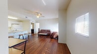 This single-floor unit offers a practical and comfortable layout across several well-defined living spaces. The living room serves as the central gathering area, featuring rich hardwood flooring, neutral white walls, and a ceiling fan overhead. Large windows fitted with horizontal blinds allow generous natural light to fill the space, creating a bright and open atmosphere. The seating area connects naturally to a dining space, reinforcing the open-concept feel.

The kitchen is equipped with white cabinetry extending to the ceiling, providing ample storage. White appliances, including a refrigerator, electric range, built-in microwave, and a double basin sink set into a peninsula counter, complete the functional cooking space. Light hardwood flooring ties the kitchen visually to the adjoining common areas.

The bedrooms feature neutral carpet flooring and windows that bring in natural light. One bedroom includes built-in shelving and a dedicated desk area, offering additional functionality. Each room provides a quiet, private retreat.

The unit includes multiple bathrooms, each finished with white tile surrounding a full soaking tub and shower combination, light tile flooring, and clean white fixtures. The consistent neutral palette throughout the unit contributes to a cohesive and understated overall aesthetic.