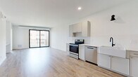Located in the heart of Minneapolis's North Loop neighborhood, this thoughtfully designed one-bedroom, one-bathroom residence offers a clean, modern aesthetic throughout. Light wood-tone flooring flows seamlessly across the entire unit, complementing the bright white walls and contemporary finishes.

The open-concept kitchen and living area serves as the heart of the home. The kitchen is outfitted with stainless steel appliances, including a range, dishwasher, and refrigerator, alongside light gray cabinetry, white subway tile backsplash, and a farmhouse-style sink with a matte black faucet. A large sliding glass door floods the living area with natural light and opens to a private balcony with views of the surrounding cityscape.

A stylish sliding barn door adds a modern-industrial touch to the entryway. The generously sized bedroom features a bold, black-framed floor-to-ceiling window that frames urban views and fills the room with natural light. The full bathroom is well-appointed with a dual-sink vanity, walk-in glass-enclosed shower with tile surround, and matte black hardware accents. A dedicated laundry area with a stacked washer and dryer adds everyday convenience, while a closet provides ample storage.