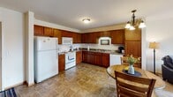 Located at 1000 Opportunity Blvd S in Cambridge, Minnesota, this single-floor residence offers a thoughtfully designed layout that balances functionality and comfort. The open-concept kitchen and dining area serves as the heart of the home, featuring rich warm-toned wood cabinetry, granite-style countertops, tile flooring, and a full suite of white appliances including a refrigerator, range, microwave, and dishwasher. A pendant chandelier illuminates the dining space, which flows naturally into the living room. The living room is carpeted and bright, benefiting from natural light streaming through a sliding glass door that opens to a private balcony with pleasant outdoor views of the surrounding landscape. The bedroom is generously sized with soft carpet, a large window that allows ample natural light, and ample space for furnishings. The full bathroom features tile flooring consistent with the kitchen, warm wood vanity cabinetry, a single-sink vanity with a broad mirror, and a tub/shower combination. A dedicated entryway with a closet provides a welcoming transition into the home. Throughout, the space maintains a clean, neutral palette that creates a warm and inviting atmosphere.