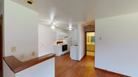 This single-floor unit offers a well-organized layout with warm hardwood flooring that flows consistently throughout the main living areas and bedrooms, creating a cohesive and inviting atmosphere. The open living area is bright and spacious, featuring a large picture window that allows natural light to fill the room, complemented by baseboard heating and clean white walls. A ceiling fan overhead adds to the comfort of the space.

The galley-style kitchen is efficiently designed, featuring white cabinetry that extends to the ceiling for ample storage, white appliances including an electric range, built-in microwave, refrigerator, and dishwasher, along with a stainless steel sink. Light countertops and hardwood flooring complete the functional cooking space. A half-wall peninsula separates the kitchen from the living area, providing an easy transition between spaces.

The bedrooms continue the hardwood flooring and maintain the clean, neutral aesthetic, each with windows that offer views of the surrounding exterior. The full bathroom is finished with white ceramic tile flooring and tiled tub surround, featuring a combined shower and bathtub, accented by warm wood-toned door frames. An additional vanity area with illuminated mirror provides added convenience. The overall ambiance of the unit is clean, practical, and move-in ready.