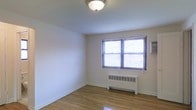 This single-floor residence offers a straightforward and functional layout with a clean, neutral aesthetic throughout. The interior is finished with warm hardwood flooring that adds a timeless character to the space, complementing the crisp white walls and bright, painted ceilings.

Natural light enters through double-hung windows dressed with horizontal blinds, lending the rooms a bright and airy feel while allowing for privacy control. A classic flush-mount ceiling fixture provides overhead lighting, keeping the space feeling open and uncluttered.

Heating is provided by a traditional cast-iron radiator positioned beneath the window, a reliable and efficient system well-suited for colder climates. The baseboards and trim are finished in white, adding a clean architectural detail that ties the room together cohesively.

The overall ambiance of the space is calm and understated, with a neutral color palette that creates a versatile canvas well-suited for a variety of furnishing styles. The simplicity of the design allows the natural materials — particularly the hardwood floors — to stand out as the defining feature of the interior. This is a practical and inviting space that balances functional living with classic residential design elements.