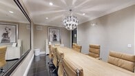Located at 45 Creekside Lane in Malvern, PA, this sophisticated conference room offers a refined and professional setting designed with attention to detail. The room is anchored by a striking live-edge natural wood conference table surrounded by tan leather executive chairs with chrome bases, providing both comfort and style for meetings and collaborative gatherings.

A standout sculptural globe chandelier serves as the visual centerpiece overhead, casting dynamic light across the coffered-style ceiling adorned with elegant crown molding. Recessed lighting complements the chandelier, ensuring the space is well-lit throughout. The floors are finished in large-format dark polished tiles, adding a sleek contrast to the warm tones of the furnishings and neutral taupe walls.

A large floor-to-ceiling mirror on one wall amplifies the sense of space and reflects the room's refined design elements. Decorative black-and-white framed artwork, including a prominent portrait, lends an upscale, contemporary aesthetic. A wall-mounted flat-screen display is positioned at one end of the table, supporting presentations and media sharing. A curved white credenza with a glass top provides additional surface space. The overall ambiance is polished and upscale, making this conference room a functional yet visually impressive space for professional use.