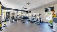Located at 1035 Alexander Dr in Augusta, Georgia, this fitness center offers a thoughtfully designed exercise space across a single floor. The room is finished with a neutral color palette of crisp white walls, crown molding, and dark rubber flooring, creating a clean and modern athletic environment.

The space is generously equipped to support a full range of workout routines. Cardio equipment includes multiple treadmills and an elliptical trainer, while strength training needs are addressed with a multi-station cable machine, a dedicated weight rack stocked with dumbbells, a weight bench, and a functional training tower complete with TRX suspension straps, medicine balls, and resistance accessories. A large mirrored wall along one side amplifies the sense of space and allows for form monitoring during exercise.

Natural light flows in through multiple windows fitted with white shutters, complemented by recessed ceiling lighting and a ceiling fan that promotes airflow throughout the room. Mounted televisions add an entertainment option for cardio sessions. Two glass-paneled entry doors provide easy access to and from the space, enhancing ventilation and connectivity to the surrounding exterior. The overall ambiance is bright, functional, and well-maintained, making it a practical and inviting environment for fitness activities.