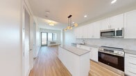 Located at 8601 Bergenline Avenue in North Bergen, NJ, this well-appointed one-bedroom, one-bathroom residence offers a thoughtfully designed open-concept layout with modern finishes throughout. The combined kitchen and living area serves as the heart of the home, anchored by a sleek center island with a gray quartz-style countertop. The kitchen is outfitted with crisp white shaker cabinetry extending to the ceiling, a subway tile backsplash, stainless steel appliances including a refrigerator, range, microwave, and dishwasher, and a modern multi-globe pendant light fixture that adds a contemporary touch. Warm-toned hardwood flooring runs throughout the entire residence, creating a cohesive and inviting atmosphere. The living area opens to a private balcony through large floor-to-ceiling windows that frame sweeping views of the New York City skyline and surrounding greenery, flooding the space with natural light. The spacious bedroom also enjoys direct balcony access and scenic views. Three closets, including a well-organized walk-in, provide generous storage. The bathroom features elegant floor-to-ceiling marble-style tile in the walk-in shower, complemented by brushed gold fixtures. An in-unit laundry area adds everyday convenience to this refined North Bergen residence.