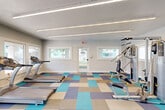 Located at 8135 N 34th Ave in Phoenix, Arizona, this fitness center offers a dedicated exercise space designed to support a well-rounded workout routine. The single-room facility is thoughtfully equipped with multiple True treadmills, an elliptical machine, and a multi-station strength training cable machine, providing options for both cardiovascular and resistance training.

The interior design strikes a clean, modern aesthetic with light gray walls and a distinctive geometric carpet in a mix of teal, blue, gray, and tan tones that adds visual energy to the space. Overhead, linear LED lighting runs across the ceiling, ensuring bright, even illumination throughout. A wall-mounted mini-split HVAC unit keeps the environment comfortable year-round.

Multiple white-framed windows line the walls, allowing natural light to flow in and offering views of the outdoor pool and surrounding property. A glass-paneled entry door features the facility's logo, contributing to a polished, branded appearance. An additional connected hallway suggests access to supplementary amenities nearby.

The layout is open and uncluttered, allowing users to move freely between equipment. Overall, this fitness center delivers a functional, modern, and inviting environment well-suited for daily exercise in the heart of Phoenix.