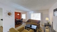 This single-story unit offers a thoughtfully designed layout that maximizes its well-proportioned footprint. The open-concept living and dining area serves as the heart of the space, creating a seamless flow between the two zones. The living room features large windows dressed with vertical blinds, allowing generous natural light to fill the room while providing views of the outdoors. Neutral-toned carpet anchors the living area, while the dining space transitions to hardwood-style flooring, adding warmth and visual contrast. A bold accent wall in the dining area introduces a rich, warm color that defines the space and adds character. An elegant pendant light fixture overhead completes the dining nook, creating an inviting atmosphere for meals. The textured ceiling adds a classic architectural detail throughout the main living areas. Together, the living and dining spaces offer a comfortable and practical environment, well-suited for everyday living and entertaining. The one-bedroom, one-bathroom configuration rounds out this efficiently designed single-floor unit.
