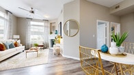 Located at 21500 Park Row Dr in Katy, TX, this single-floor residence offers a thoughtfully designed layout with a warm, contemporary aesthetic throughout. The living room serves as the heart of the home, anchored by a striking white-surround fireplace and framed by large windows that invite abundant natural light. Wood-look flooring flows seamlessly throughout the space, complementing the neutral taupe and warm white color palette.

The kitchen is outfitted with crisp white cabinetry, a subtle tile backsplash, and a full suite of stainless steel appliances, including a refrigerator, range, microwave, and dishwasher. A cozy dining nook adjacent to the kitchen provides a functional everyday eating area.

A secondary flexible space with a walk-in closet offers utility as a home office or sitting room. The bedroom features a spacious closet and a calm, restful ambiance. The bathroom is finished with white shaker-style cabinetry, stone-look countertops, and brushed nickel hardware.

A hallway connects the rooms efficiently, enhanced by a decorative round mirror that adds visual depth. The overall design balances practicality with an inviting, modern character well-suited to comfortable everyday living.