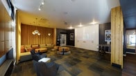 This single-floor space serves as a contemporary communal lounge and screening room, thoughtfully designed to accommodate both casual socializing and media viewing. The room is divided into distinct zones that together create a versatile, engaging environment.

The screening area is anchored by a large, dedicated projection wall that dominates one side of the room, painted in a clean white against a contrasting dark charcoal surround. A ceiling-mounted projector ensures a quality viewing experience, while framed artwork adds a gallery-like touch to the surrounding walls.

The lounge area is defined by warm, golden tones introduced through floor-to-ceiling vertical wood slat panels and rich amber-hued sofas and low-profile sectional seating. Pendant lighting with metallic globe fixtures hangs overhead, casting a warm, intimate glow that complements the track lighting above.

Seating throughout the space is varied, featuring low wooden coffee tables, modular floor cushions, and upholstered armchairs arranged to encourage both group gatherings and individual relaxation. A small high-top table and bar-height seating are positioned to one side for added functionality.

The patterned carpet tiles ground the space with a modern aesthetic while adding texture underfoot, contributing to the room's overall polished, contemporary ambiance.