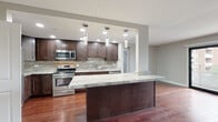 Located at 21 Kristin Dr in Schaumburg, Illinois, this single-floor residence offers a thoughtfully updated interior defined by rich hardwood flooring that flows consistently throughout the living spaces. The open-concept kitchen is a standout feature, showcasing dark espresso cabinetry, striking marble-veined granite countertops, a full marble tile backsplash, and stainless steel appliances including a gas range and built-in microwave. A large central island with pendant lighting above provides additional prep and seating space, while recessed lighting ensures a bright, welcoming atmosphere. The expansive living area connects seamlessly to the kitchen and opens to a private balcony through a sliding glass door, offering pleasant outdoor views and an abundance of natural light. The bedrooms are generously proportioned, each featuring hardwood floors, large windows with natural light, and ample closet space. The bathrooms have been fully updated with large-format tile work, glass-enclosed showers, a soaking tub option, granite vanity countertops, and dark wood cabinetry that complements the overall design aesthetic. Neutral gray tones on the walls throughout create a clean, modern palette that ties the entire space together cohesively.
