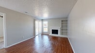 This single-floor, 1-bedroom, 2-bathroom residence offers a well-utilized layout designed for efficient everyday living. The open-plan kitchen and living area serves as the heart of the home, featuring rich hardwood flooring, neutral gray walls, and a textured popcorn ceiling. A white-brick wood-burning fireplace anchors the living space, flanked by built-in open shelving that provides both display and storage opportunities. Natural light enters through windows fitted with vertical and horizontal blinds, lending a bright and airy feel to the common areas.

The bedroom is carpeted for comfort and includes a window with blinds that allows natural light to filter in. The room connects conveniently to one of the two bathrooms, which features a vanity with blue cabinetry, providing a subtle pop of color. Three closets throughout the unit offer generous storage capacity relative to the overall footprint.

The kitchen shares its space with the living area in an open-concept arrangement, maximizing the sense of space within the compact floor plan. The neutral color palette used throughout the unit creates a cohesive and clean aesthetic. Overall, this residence delivers a functional and comfortable living environment, with notable features such as the fireplace, built-in shelving, and dual bathrooms making it a practical and characterful home.
