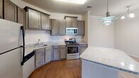 Located at 100 Hamilton Ridge Dr in Alcoa, Tennessee, this single-floor home offers a well-designed, open layout with a neutral color palette and a blend of hardwood-style and plush carpeted flooring throughout. The kitchen is a functional highlight, featuring rich gray cabinetry, granite-style countertops, stainless steel appliances including a range, microwave, refrigerator, and dishwasher, along with a peninsula that provides additional prep and dining space. A pendant light fixture adds a polished finishing touch to the kitchen area.

The living areas are bright and inviting, with crown molding accenting the walls and an abundance of natural light filtering through large windows dressed with blinds. The spacious bedrooms are carpeted for comfort, with one bedroom featuring an oversized walk-in closet outfitted with wire shelving on multiple walls, offering excellent organizational capacity.

The bathroom includes a full-size soaking tub with a tiled surround and built-in corner shelving. A dedicated laundry room accommodates full-size side-by-side washer and dryer units with overhead wire shelving for added storage. Clean white doors, consistent trim work, and thoughtful finishes contribute to the home's cohesive, move-in-ready character throughout.