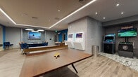 Located at 1000 Schindler Dr in South Amboy, NJ, this single-floor recreational amenity space is thoughtfully designed to offer a wide variety of entertainment options in a modern, energetic environment. The interior is finished with light hardwood-style flooring, recessed and linear LED ceiling lighting, and bold blue accent walls adorned with eclectic artwork, creating a lively yet polished ambiance throughout.

The space is anchored by a full-size ping-pong table and a shuffleboard table positioned along a vibrant blue wall. A dedicated arcade corner houses multiple classic arcade cabinets alongside wall-mounted interactive gaming kiosks, all set against a geometric patterned feature wall. A large flat-screen display adds to the entertainment experience in the main lounge area, which is furnished with plush seating, round tables, and stylish chairs ideal for socializing.

A standout feature is the enclosed golf simulator room, complete with a full projection screen, synthetic turf hitting mat, and a dedicated control station — offering a fully immersive virtual golf experience. Adjacent areas provide comfortable lounge seating with warm, curated furnishings.

Throughout the space, the combination of bold color choices, curated art pieces, varied gaming offerings, and flexible seating arrangements makes this a well-rounded, community-focused recreational destination.