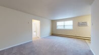 This single-floor residence offers a practical and comfortable layout designed to maximize livability across its key spaces. The galley-style kitchen is outfitted with dark-toned cabinetry, light wood-look vinyl plank flooring, and a full suite of white appliances including a gas range, over-the-range microwave, and full-size refrigerator — providing efficient functionality in a compact footprint.

The living area is generously proportioned, featuring wall-to-wall carpet, neutral warm-toned walls, and a large window that draws in natural light. Baseboard heating runs throughout the unit, ensuring consistent warmth. An open doorway connects the living space to adjacent rooms, contributing to an easy flow throughout.

The bedrooms are well-sized with plush carpeting, window blinds for privacy, and baseboard heating. One bedroom features two reach-in closets, offering notable storage capacity. Another bedroom is equipped with a wall-mounted air conditioning unit for individual climate control.

The bathroom is clean and bright, featuring a full soaking tub with a tiled shower surround, a modern vanity with a wood-toned cabinet base, and a white undermount sink with polished chrome fixtures. The overall palette throughout the residence is light and neutral, creating a calm and move-in-ready atmosphere.