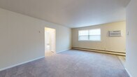 This single-floor residence offers a practical and comfortable layout designed to maximize livability across its key spaces. The galley-style kitchen is outfitted with dark-toned cabinetry, light wood-look vinyl plank flooring, and a full suite of white appliances including a gas range, over-the-range microwave, and full-size refrigerator — providing efficient functionality in a compact footprint.

The living area is generously proportioned, featuring wall-to-wall carpet, neutral warm-toned walls, and a large window that draws in natural light. Baseboard heating runs throughout the unit, ensuring consistent warmth. An open doorway connects the living space to adjacent rooms, contributing to an easy flow throughout.

The bedrooms are well-sized with plush carpeting, window blinds for privacy, and baseboard heating. One bedroom features two reach-in closets, offering notable storage capacity. Another bedroom is equipped with a wall-mounted air conditioning unit for individual climate control.

The bathroom is clean and bright, featuring a full soaking tub with a tiled shower surround, a modern vanity with a wood-toned cabinet base, and a white undermount sink with polished chrome fixtures. The overall palette throughout the residence is light and neutral, creating a calm and move-in-ready atmosphere.