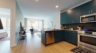 Located at 100 Water Street in Jersey City, this single-floor residence offers a thoughtfully designed open-concept layout that seamlessly connects the kitchen, dining, and living areas. Light wood flooring runs throughout, lending warmth and continuity to the space.

The kitchen is a standout feature, showcasing bold teal cabinetry paired with a dark mosaic tile backsplash and stainless steel appliances, including a full-size refrigerator, range, microwave, and dishwasher. A peninsula with a built-in sink bridges the kitchen to the living area, making it well-suited for both daily use and entertaining.

The living and dining area is bright and airy, benefiting from floor-to-ceiling windows dressed with neutral roller shades and flowing curtains. A sculptural pendant light anchors the dining space, while the living area offers comfortable seating and views of the surrounding neighborhood.

The two bedrooms are calm and understated, each featuring large windows that bring in natural light and outdoor views, along with light wood flooring and ample closet storage. The bathroom is clean and minimal, featuring a glass-enclosed walk-in shower with white tile surround and chrome fixtures.