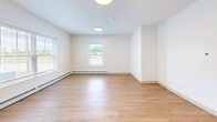 Located at 8 Admiral Harry Rich Dr in Brunswick, Maine, this single-floor, one-bedroom, one-bathroom unit offers a well-designed layout that maximizes its compact footprint. Light-toned hardwood-style flooring runs throughout the main living areas, complementing the bright white walls and flush-mount ceiling lighting that keep the space feeling open and airy.

The combined kitchen and living area serves as the heart of the unit. The kitchen is equipped with stainless steel appliances — including a refrigerator, range, and microwave — set against rich, dark-toned cabinetry with light countertops. A peninsula provides additional prep space and acts as a natural divider between the kitchen and living area. A wall-mounted mini-split unit ensures efficient climate control, supplemented by baseboard heating along the perimeter walls. Windows allow natural light to filter in with views of the surrounding greenery.

A bright hallway connects the main living space to the bedroom and bathroom. The bedroom features soft, neutral-toned carpet, light blue-gray walls, a sliding double-door closet, and a window that brings in natural light. The bathroom is clean and functional, with a dark-toned vanity, white countertop, and a full tub/shower combination with grab bars, finished with hardwood-style flooring.