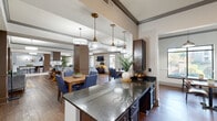 Located at 8500 Franciscan Woods Dr in Columbus, Georgia, this generously sized single-floor space offers a thoughtfully designed open-concept layout that seamlessly connects its key areas. The kitchen is outfitted with rich dark-wood cabinetry, granite countertops, a tile backsplash, and full-sized black appliances, including a side-by-side refrigerator. A large island provides additional prep and serving space, flowing naturally into the adjacent dining and living areas. The dining room features a warm wooden table surrounded by upholstered blue chairs, lit by stylish pendant lighting and framed by decorative wall art. The expansive living room is anchored by a large sectional sofa, hardwood flooring, tray ceilings with crown molding, and a wall-mounted flat-screen TV. Large windows throughout the space invite abundant natural light and offer views of the surrounding landscape. A cozy lounge nook with built-in banquette seating and additional seating areas with leather chairs provide versatile gathering spots. The space extends further to include a billiards table, making it well-suited for social and recreational use. Consistent hardwood flooring, neutral tones, and elevated ceiling details contribute to a cohesive and welcoming ambiance throughout.