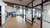 Located at 1101 N Main St in Los Angeles, this contemporary fitness center is designed to deliver a complete and energizing workout experience across a single, well-organized floor. The space is defined by soaring ceilings, floor-to-ceiling windows along the perimeter, and an abundance of natural light that creates an open, airy atmosphere throughout.

The main workout area is generously proportioned and divided into distinct functional zones. A dedicated cardio section houses a row of Matrix treadmalls, stair climbers, and ellipticals, all positioned to take advantage of the expansive outdoor views. Adjacent to this, a comprehensive strength training area features cable machines, multi-functional racks, free weights, adjustable benches, and wall-mounted mirrors to support a full range of resistance exercises.

A glass-partitioned studio room provides an intimate space for cycling classes, equipped with Matrix stationary bikes and supplementary fitness accessories. The entryway transitions smoothly into the facility through a corridor accented by a bold, colorful cityscape mural that adds a vibrant urban character to the space.

Durable rubber flooring runs throughout, complementing the industrial-modern aesthetic defined by dark steel framing, exposed brick accents, pendant lighting, and mounted flat-screen televisions. The overall design balances functionality with a polished, motivating ambiance suited for a diverse range of fitness activities.