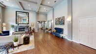 Located at 8531 Summersweet Ln in Raleigh, NC, this single-floor community space is thoughtfully designed to blend comfort and functionality. The open-plan layout seamlessly connects the living and dining areas, creating a welcoming environment for socializing and gathering.

The living area is anchored by dramatic double-height ceilings that amplify the sense of openness, while rich hardwood flooring runs throughout, adding warmth and continuity. A cozy fireplace with a brick surround anchors one end of the living space, complemented by elegant coffered ceiling details and recessed lighting. Large French doors with transom windows above flood the room with natural light and provide direct views and access to an outdoor pool area, blurring the line between interior and exterior living.

The dining area features a striking granite-topped curved bar with bar seating, a round glass-top bistro table, and a sculptural globe chandelier overhead. Teal-accented ceiling recesses add a bold pop of color, while built-in shelving and mounted displays enhance the functional design. An adjacent kitchenette with stainless steel appliances supports the space's entertaining capabilities.

Throughout, curated wall art, sconce lighting, and large windows overlooking lush greenery contribute to a refined yet approachable ambiance, making this a versatile and visually engaging communal space.