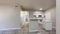 This single-story, 4-bedroom, 2-bathroom home offers a practical and well-organized layout designed to maximize comfort and functionality. The open-concept living, dining, and kitchen area serves as the heart of the home, featuring light gray wood-look flooring that creates a clean, cohesive aesthetic throughout the common spaces. The kitchen is equipped with white cabinetry, a white range, and a central island topped with a marble-look countertop, providing both additional prep space and a natural gathering point. The living area benefits from natural light via windows with blinds and includes a dedicated entry door.

The four bedrooms are carpeted for warmth and comfort, each featuring windows with blinds that allow for natural light. Each bedroom is paired with its own closet, including a notably spacious walk-in closet outfitted with wire shelving systems for organized storage. The two full bathrooms each include a tub-shower combination, a white vanity with marble-look countertops, and wood-look tile flooring, maintaining a consistent, clean design throughout. A dedicated hallway connects the private areas of the home, and an in-unit laundry space adds everyday convenience. Neutral gray walls and white trim tie the entire space together with a bright, understated palette.