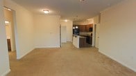 Located at 900 Old Fashioned Way in Newport, NC, this single-floor residence offers a thoughtfully designed open-concept layout that seamlessly blends the living and kitchen areas into one cohesive space. The living area is generously sized, finished with neutral wall-to-wall carpeting that adds warmth and comfort underfoot. Crown molding runs along the ceiling, lending a clean, polished architectural detail throughout. The kitchen is a functional centerpiece of the home, featuring rich wood cabinetry, dark countertops, and a suite of black appliances including a refrigerator, microwave, and range. A kitchen island with pendant lighting above serves as both a prep area and a casual gathering point, while track lighting provides additional illumination across the workspace. The open sightlines between the kitchen and living area create a sense of expansiveness, making the space feel bright and connected. Interior doors provide access to additional rooms, suggesting a practical and well-organized floor plan. The overall ambiance is clean, neutral, and move-in ready, offering a comfortable and functional living environment suited for everyday life in Newport, NC.